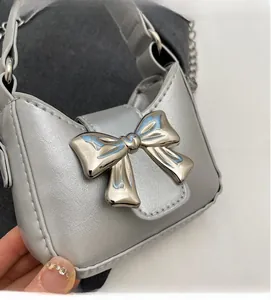 Close-up of silver mini crossbody bag with a large metallic bow and delicate chain strap