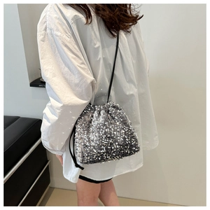 Détail d'un sac seau à paillettes argentées avec cordon porté sur une chemise blanche