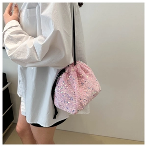 Détail du sac seau à paillettes roses avec cordon de serrage sur une chemise blanche