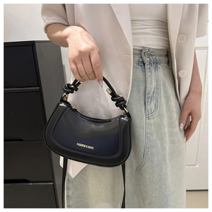 Detail of black semi-circle handbag with knot handle and detachable crossbody strap