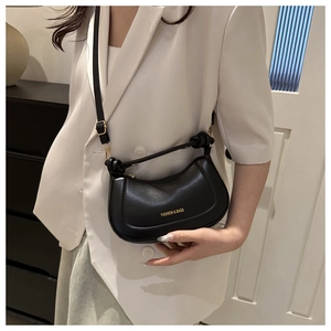 Fashionable black crescent shoulder bag shown on a model in a white blazer