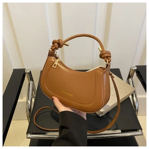 Detailed close-up of a caramel crescent handbag with a unique knotted top handle design