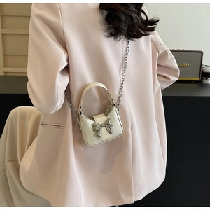 Chic cream mini bow handbag with silver chain strap shown worn by a model in a cozy cafe