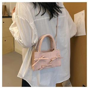 Pink matte crossbody bag with bow details worn by a model in a minimal lifestyle setting