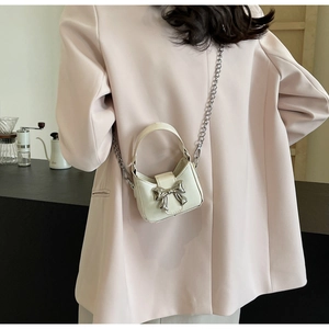 Detailed view of a white mini bag featuring a silver bow buckle and elegant metal chain