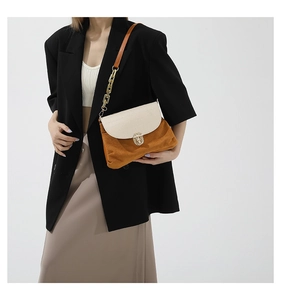 Detail of a chic patchwork shoulder bag with metal clasp and chain strap on a model