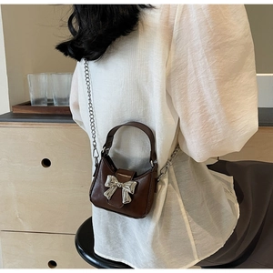 Close-up of small dark brown leather bag featuring a silver bow buckle and metal chain