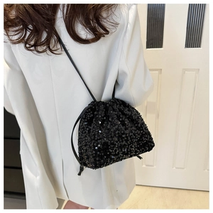 Détail du sac seau noir à paillettes avec cordon sur fond de blazer blanc élégant