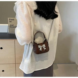 Detailed view of a brown mini handbag with silver metal bow and chain strap on a model