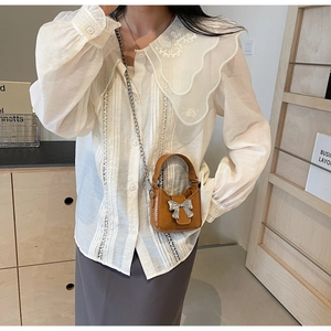 Detail of a brown mini handbag with a silver metallic bow and elegant chain strap