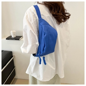Detail of royal blue canvas crossbody chest bag with woven zipper pull on casual outfit