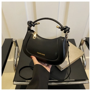 Detail of black semi-circular handbag featuring a unique knotted handle and gold hardware