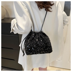 Détail d'un sac seau noir à paillettes avec cordon porté à l'épaule sur un blazer blanc
