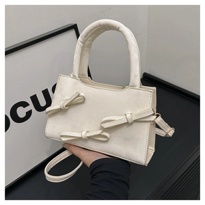 Detail of a creamy white handbag featuring three elegant bows and a sturdy top handle
