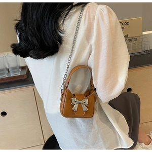Detailed view of mini brown leather handbag with silver metallic bow and chain strap