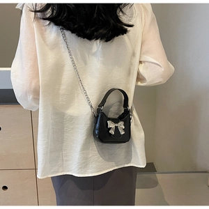 Detail of black mini crossbody bag with silver bow accent and metal chain on a model