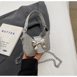 Detail of silver gray mini handbag featuring a metallic bow accent and delicate chain strap