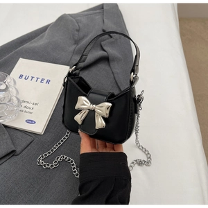 Close-up of black mini handbag with silver metal bow and delicate chain shoulder strap