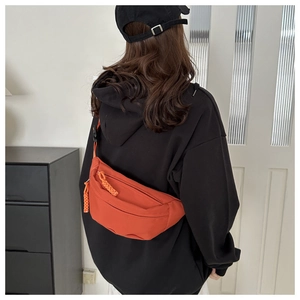Detail view of a vibrant orange nylon crossbody chest bag worn over a black hoodie