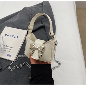 Detail of a creamy white mini handbag with silver metal bow and fine chain strap