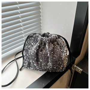 Détail d'un sac seau à paillettes argentées avec cordon en cuir noir sur un rebord de fenêtre