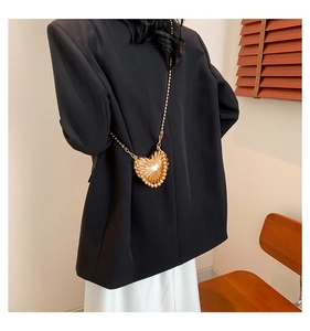 Vista dettagliata di una mini borsa a cuore dorata con catena su un blazer nero