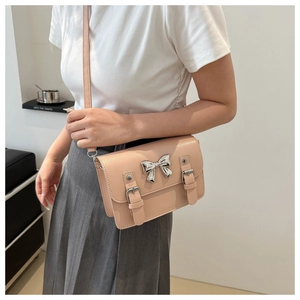 Detail view of beige crossbody bag featuring silver bow hardware and decorative belt straps