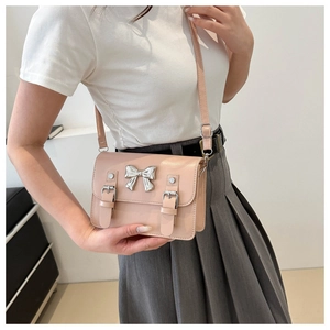 Detail of soft pink glossy crossbody bag with silver bow accent and adjustable straps