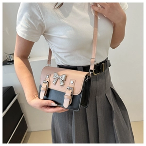 Detail of pink and black crossbody bag with silver bow accent and buckle straps