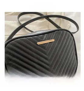 Detailed view of black quilted leather camera bag with elegant V-shaped stitching and gold hardware