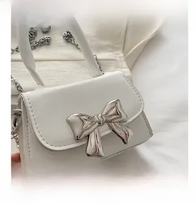 Detail view of a white mini handbag featuring a silver metallic bow and chain strap