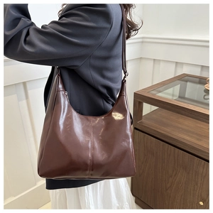 Close-up of a dark brown glossy leather crescent shoulder bag worn by a model