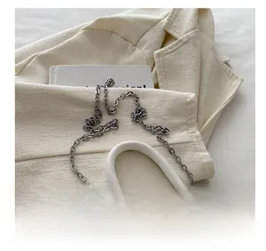 Close-up of white PU leather handbag with silver metal bow and delicate chain strap