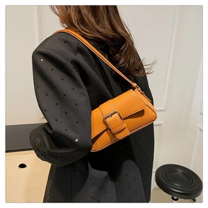 Detail of orange baguette shoulder bag with decorative buckle on model with black blazer