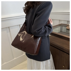 Detail of glossy chocolate brown leather tote bag worn with a stylish grey blazer