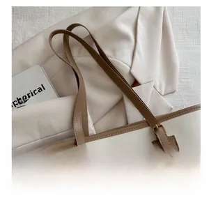 Detail of soft cream tote bag featuring brown leather trim and metallic adjustment buckle