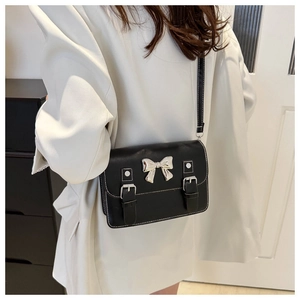 Detail showing a black crossbody bag with a silver bow and white contrast stitching