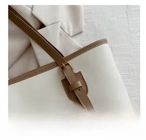 Detail view of beige tote bag with brown leather trim and golden metal buckle