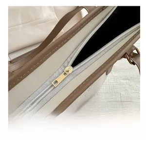Close-up of smooth gold metal zipper and stitching on a textured beige leather tote bag