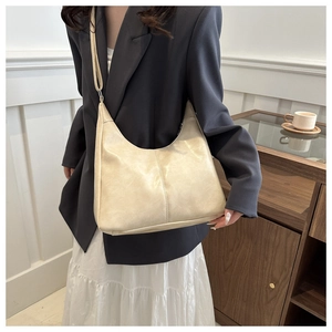 Detail view of a cream-colored half-moon hobo bag styled with a professional blazer