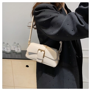 Close-up of cream leather shoulder bag featuring a prominent gold square buckle and strap