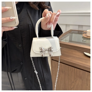Close-up of a white mini handbag featuring a silver metal bow buckle and a fine chain strap