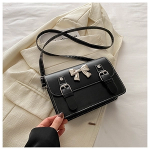 Detail of black crossbody bag with white stitching and silver bow metal buckle