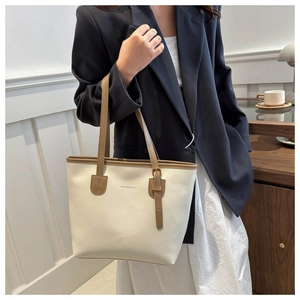 Detail of minimalist cream tote bag with brown leather straps worn by model