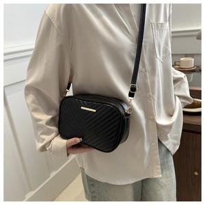 Detail of black crossbody bag featuring V-shaped quilting and golden metal accent decor