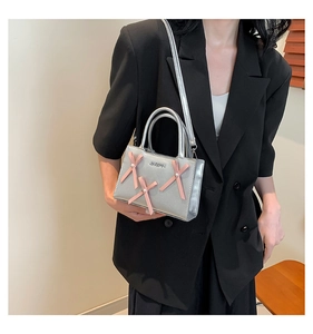 Petit sac carré argenté avec nœuds roses et perles porté sur une veste noire