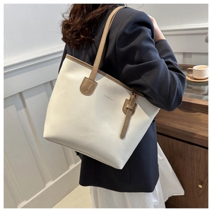 Detail of a large white tote bag with brown handles worn on the shoulder for commuting