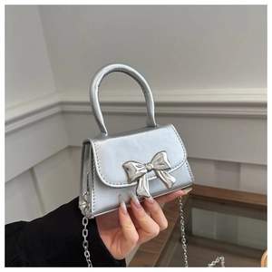 Detail of silver mini handbag with metallic bow decoration and chain strap shown by a model