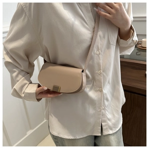 Detail view of the elegant beige leather saddle bag featuring a gold striped buckle fastener