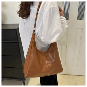 Close-up of brown glossy PU leather tote bag worn as a shoulder bag on a model